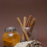 Various spices including turmeric and cinnamon displayed in glass containers with sesame and asafoetida on a brown background.