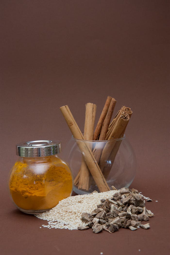 Services Various spices including turmeric and cinnamon displayed in glass containers with sesame and asafoetida on a brown background.
