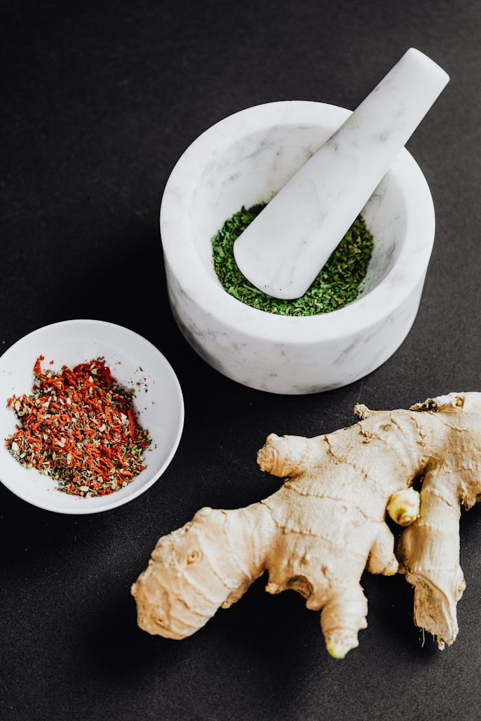 Services Flat lay of fresh ginger root, herbs, and spices with marble mortar and pestle on dark background.