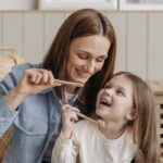 A mother and daughter enjoying quality time while brushing their teeth together indoors.