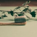Wooden toothbrush with toothpaste against a plant background, emphasizing natural oral care.